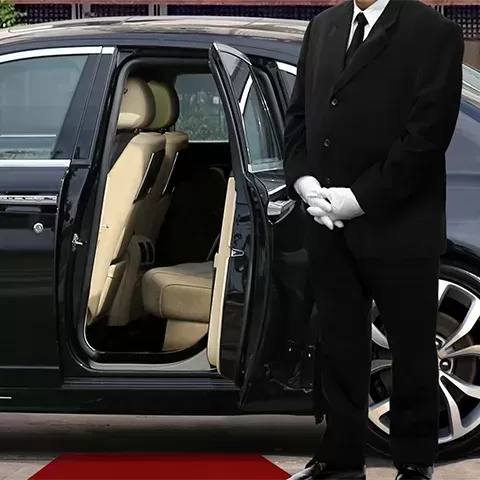 Chauffer in suit and gloves standing outside of car with passenger door open