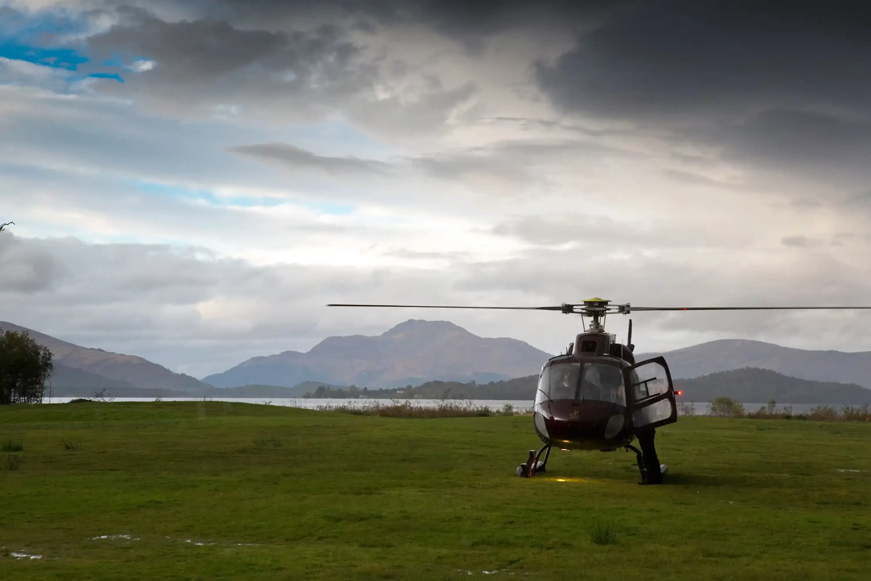 Helicopter on grass field with gloomy sky and mountain scenery