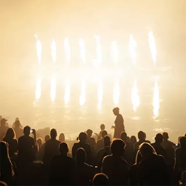Dim lit photo of people gathering in a crowd in front of a lit up stage