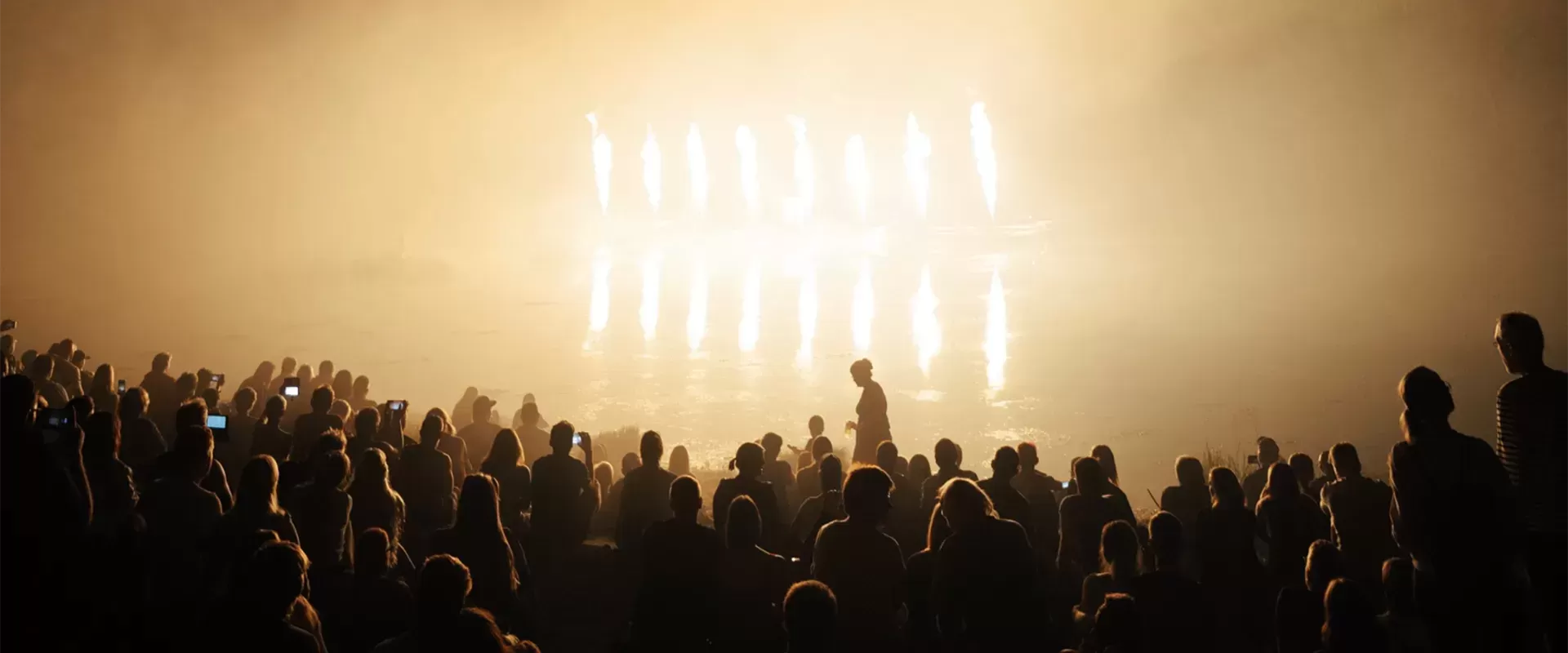 Dim lit photo of people gathering in a crowd in front of a lit up stage