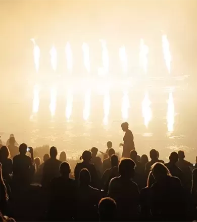 Dim lit photo of people gathering in a crowd in front of a lit up stage