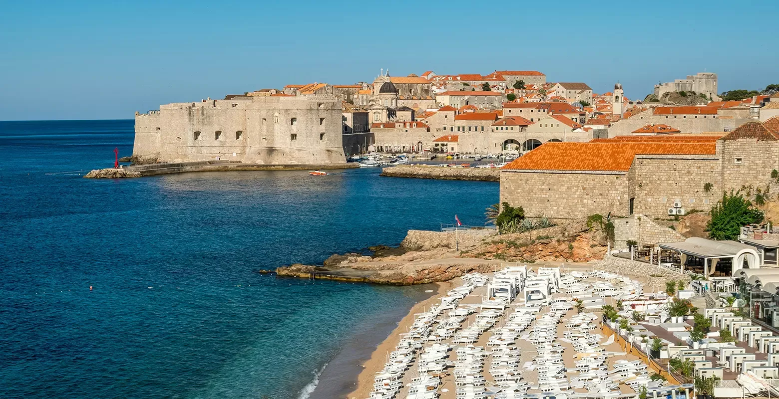 The picturesque beach of Dubrovnik, Croatia, featuring golden sands and vibrant blue sea under a clear sky.