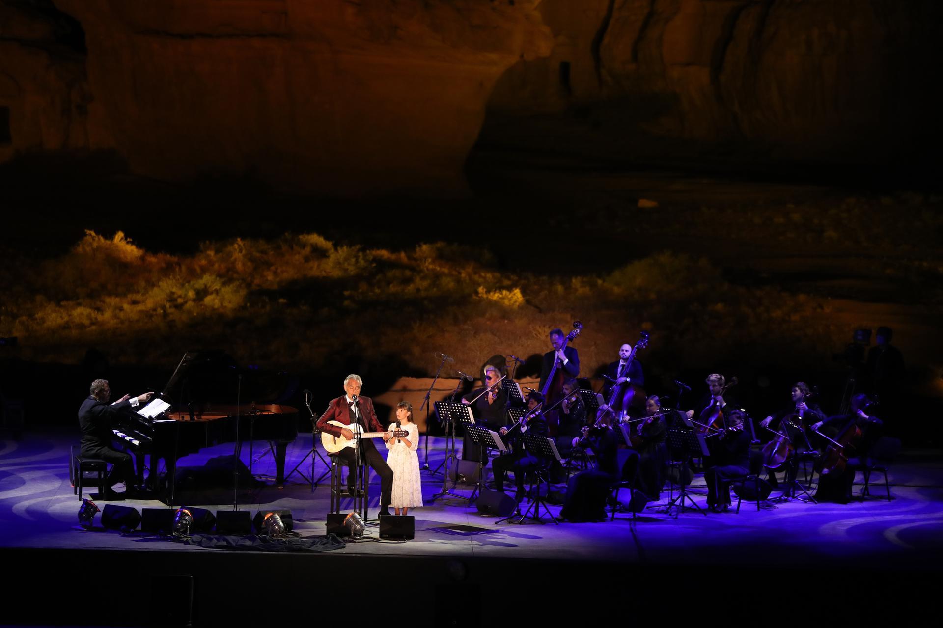 Outside stage performance orchestra, piano player, man in red suit playing guitar and girl in dress signing