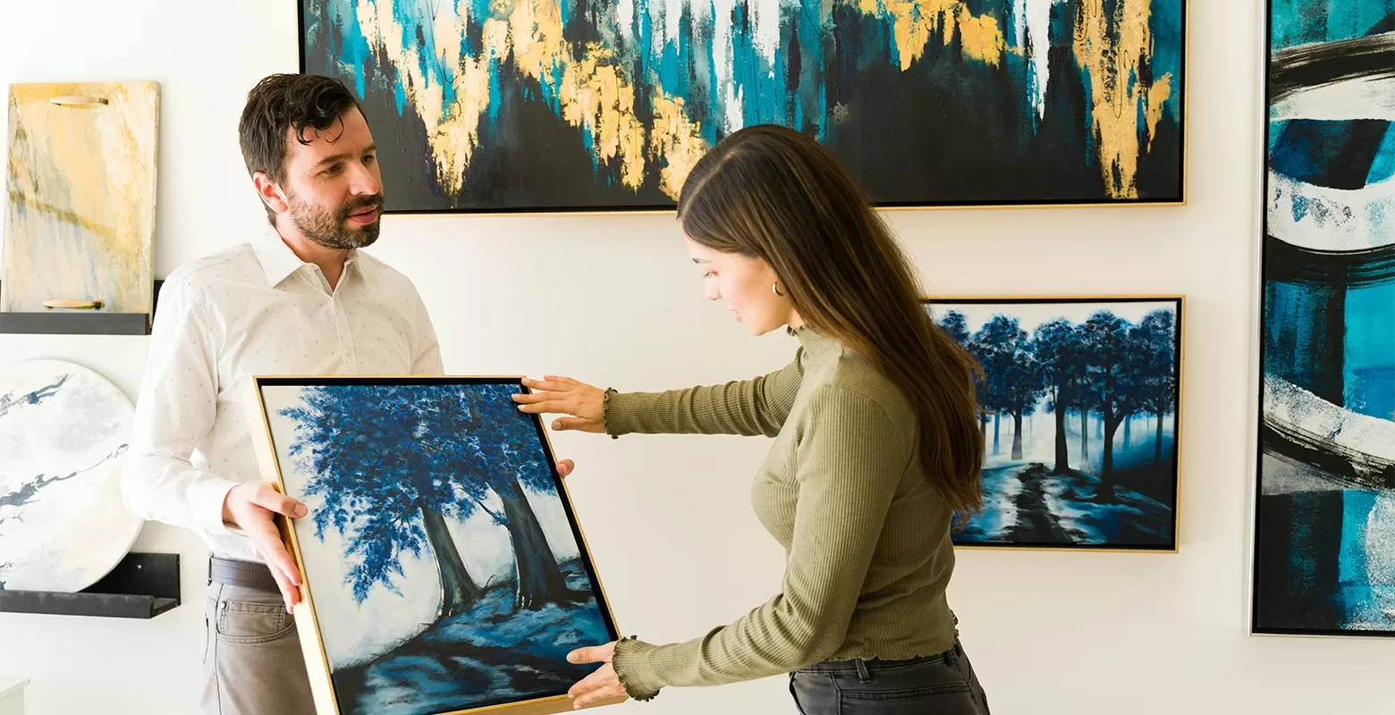 A man and woman observe artwork together in a gallery, engaged in discussion about the pieces on display.