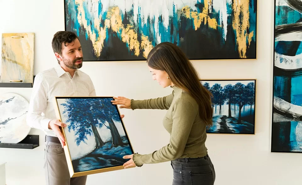 A man and woman observe artwork together in a gallery, engaged in discussion about the pieces on display.