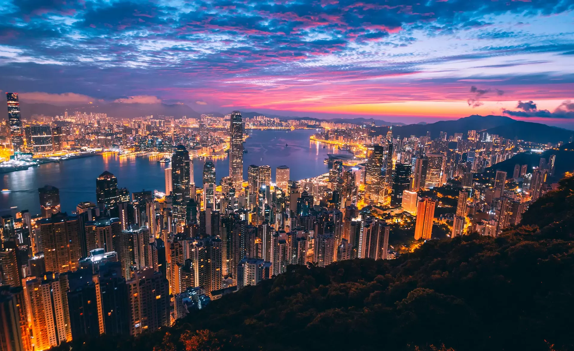 A stunning view of the Hong Kong skyline illuminated by the warm hues of sunset, showcasing iconic skyscrapers against the sky.