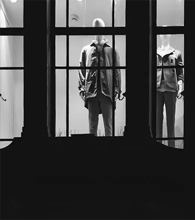Black and white photo of window display of mannequins wearing men and women's fashion