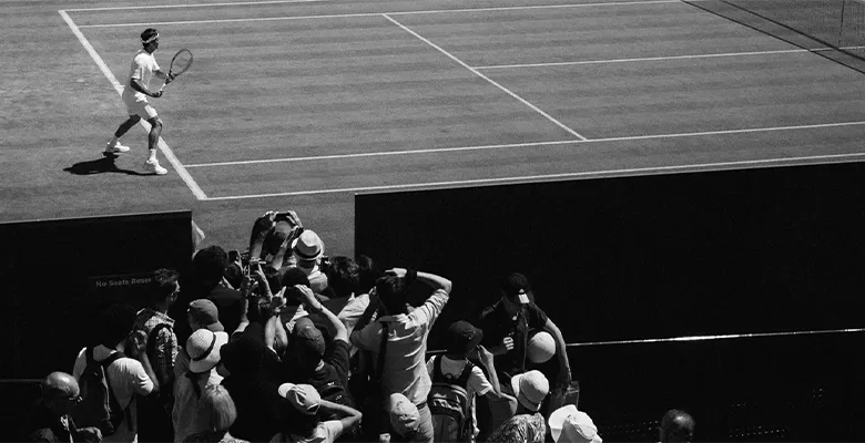 Man playing tennis as a crowd watch from the side of the court.