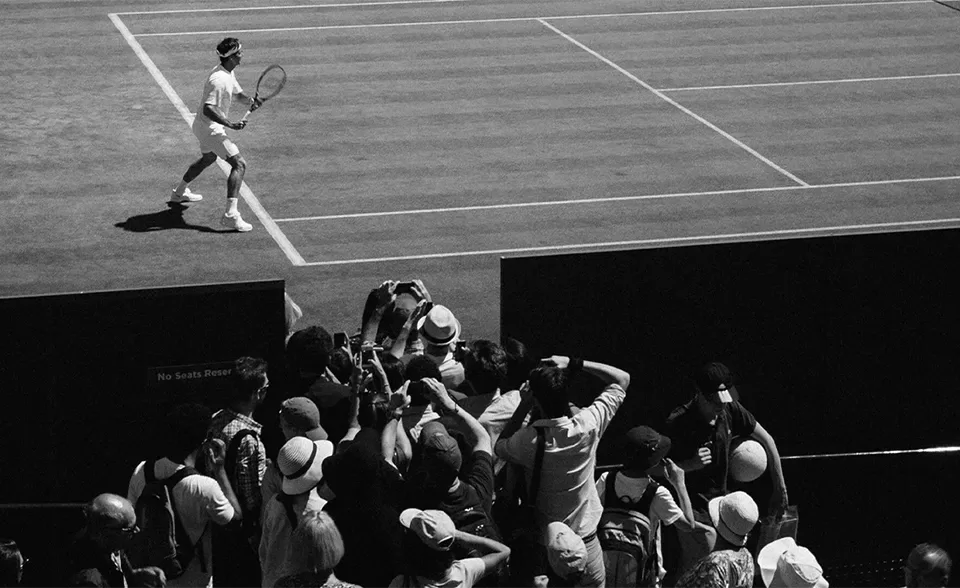 Man playing tennis as a crowd watch from the side of the court.