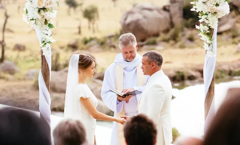 Bridge and groom holding hands at wedding ceromony with the priest as viewers watch | Quintessentially Weddings