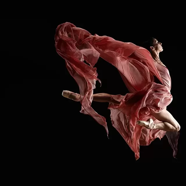 Professional photo of beautiful ballet dancing in an in-air pose with her red dress draped and flowing in the air.