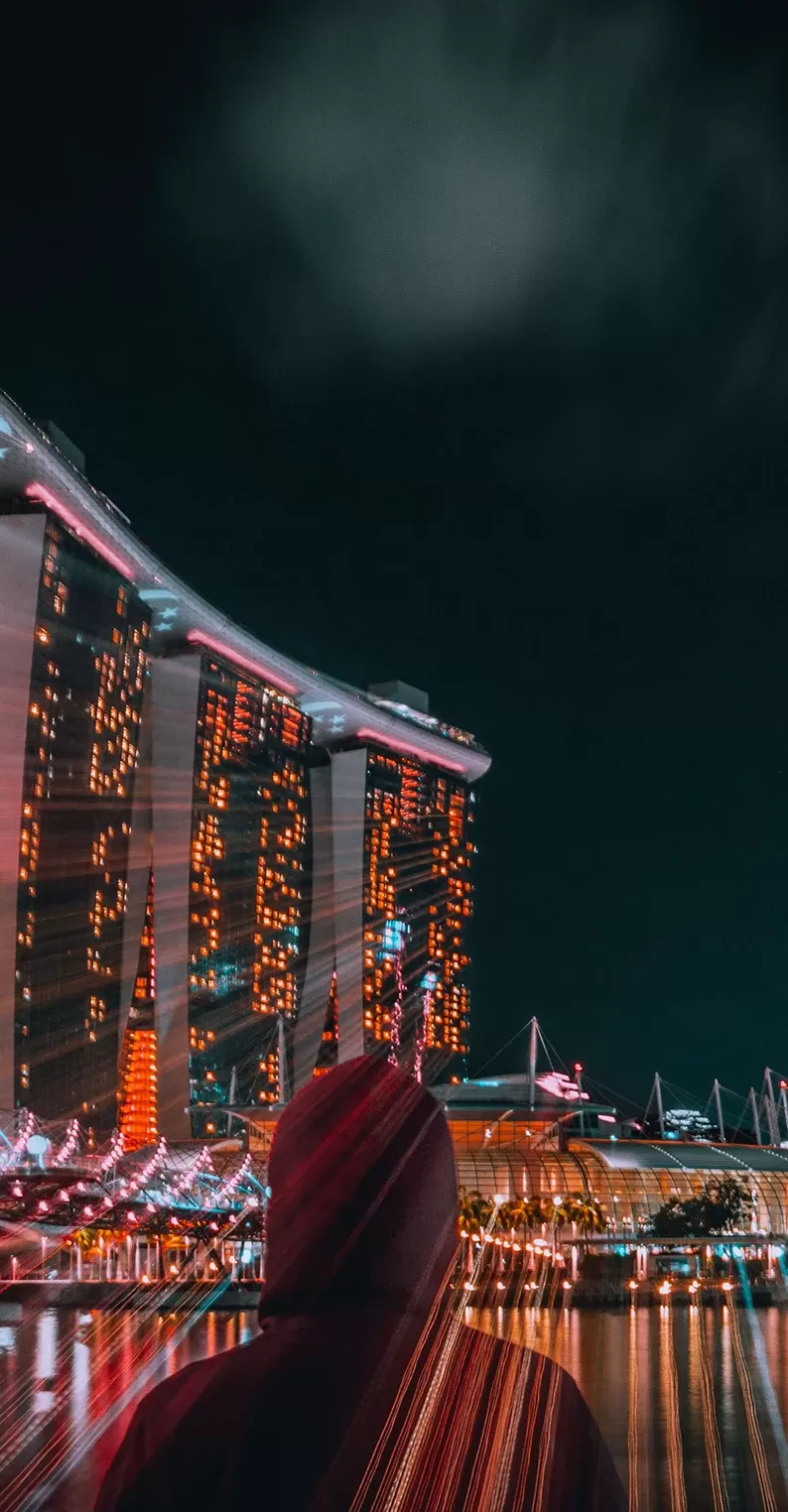 Person wearing a red hoodie looking across the river at the lit up city of Singapore