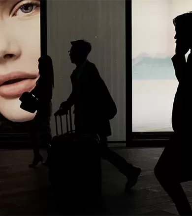 Black silhouettes of people walking in front of colourful adverts on a building