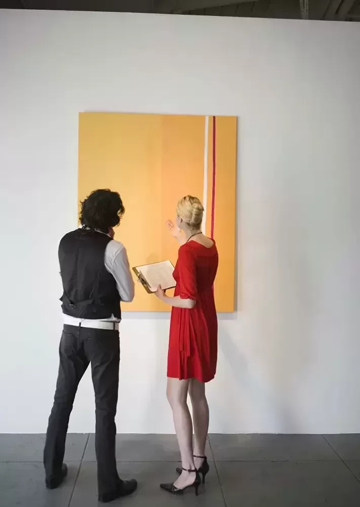 Two people observing art on a wall in a gallery.