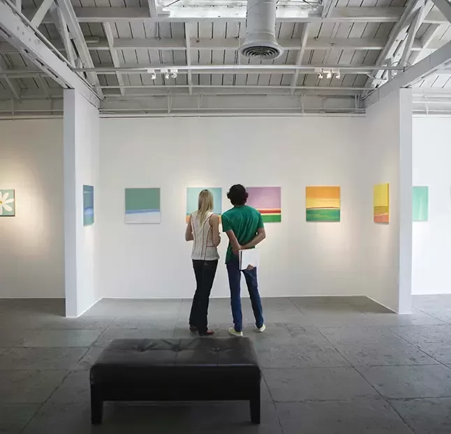 Two people observing colourful art on a wall in a gallery.