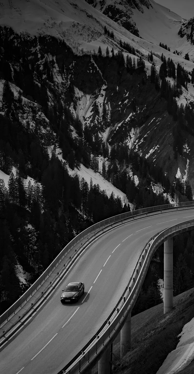 Jaguar car driving on bridge road between snowy mountains