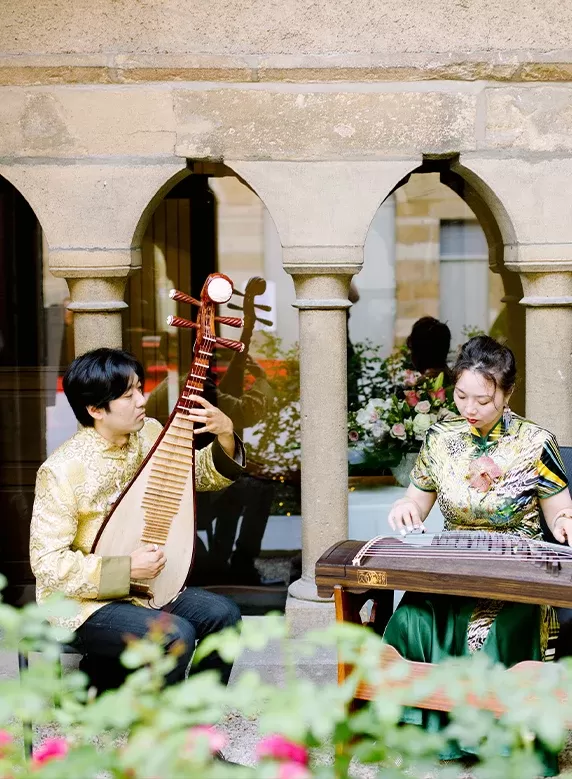 Couple sat outside playing string intruments in beautiful printed mandarin collar tops | Quintessentially Weddings