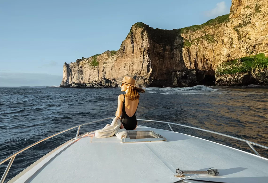 A woman perched on the bow of a boat, taking in the tranquil scenery and the soothing sounds of the water.