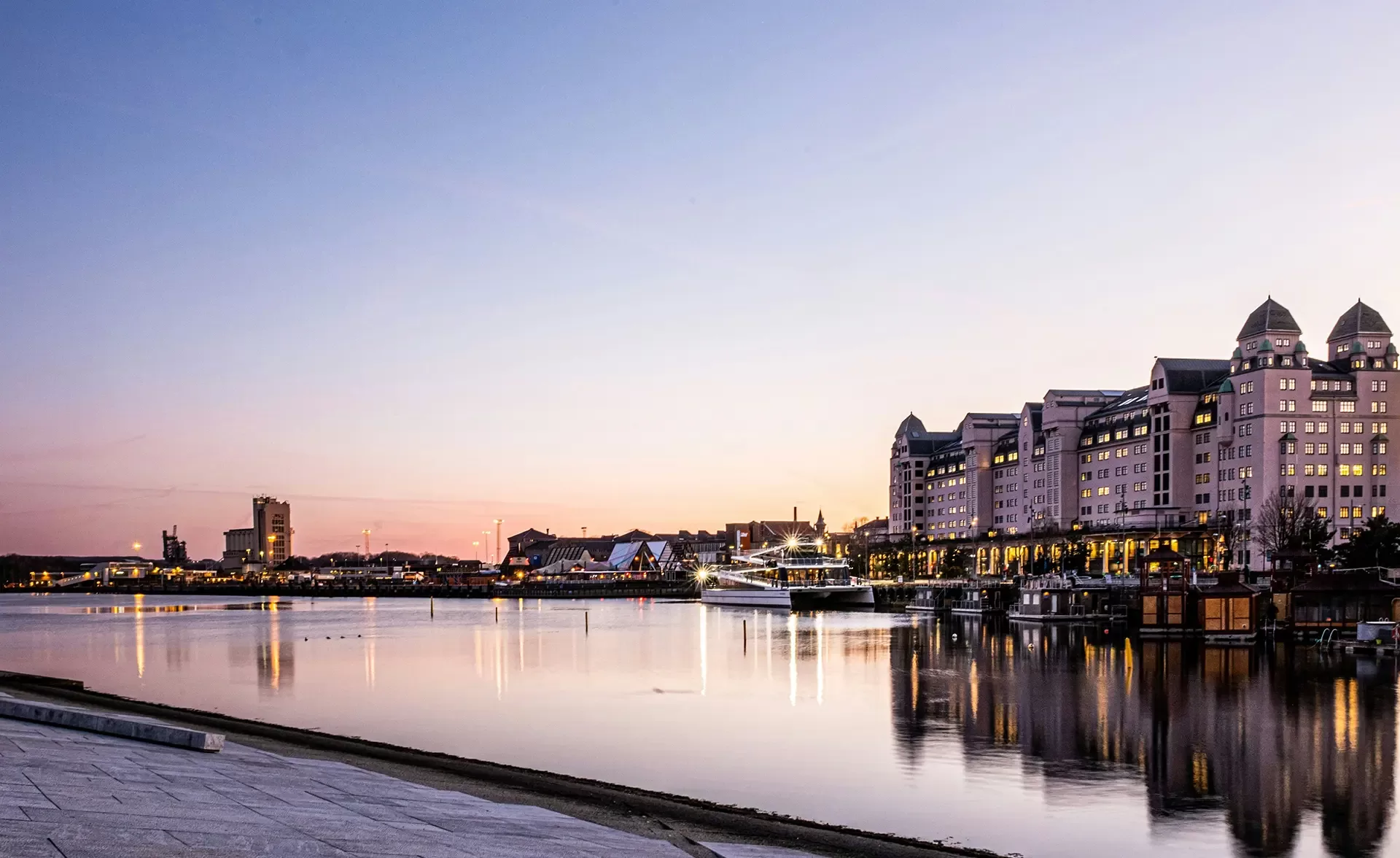 Oslo skyline at dusk, featuring a serene river and illuminated buildings reflecting the evening light.