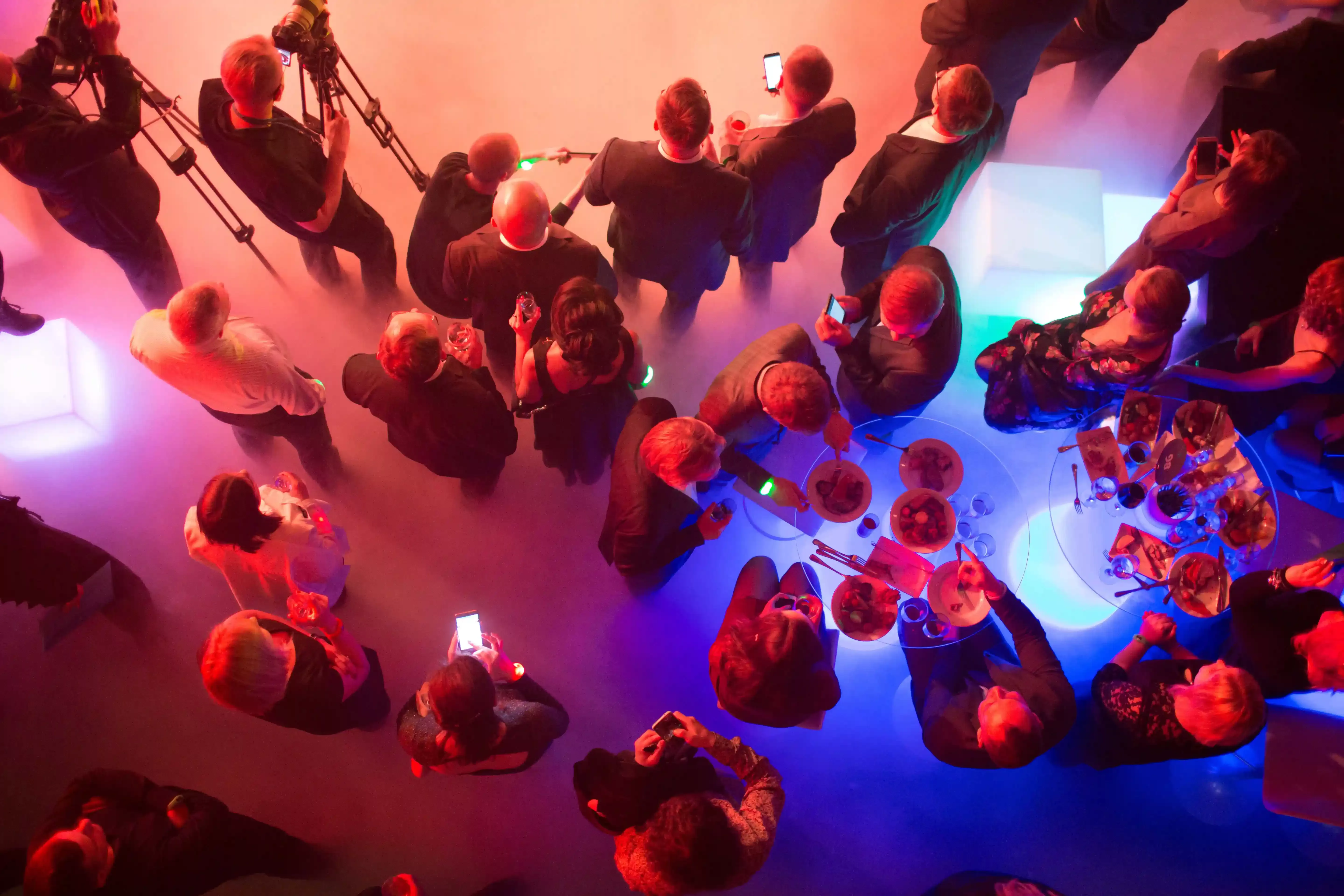 Birdseye view of people standing drinking and socialising in the colourful lit-up room.