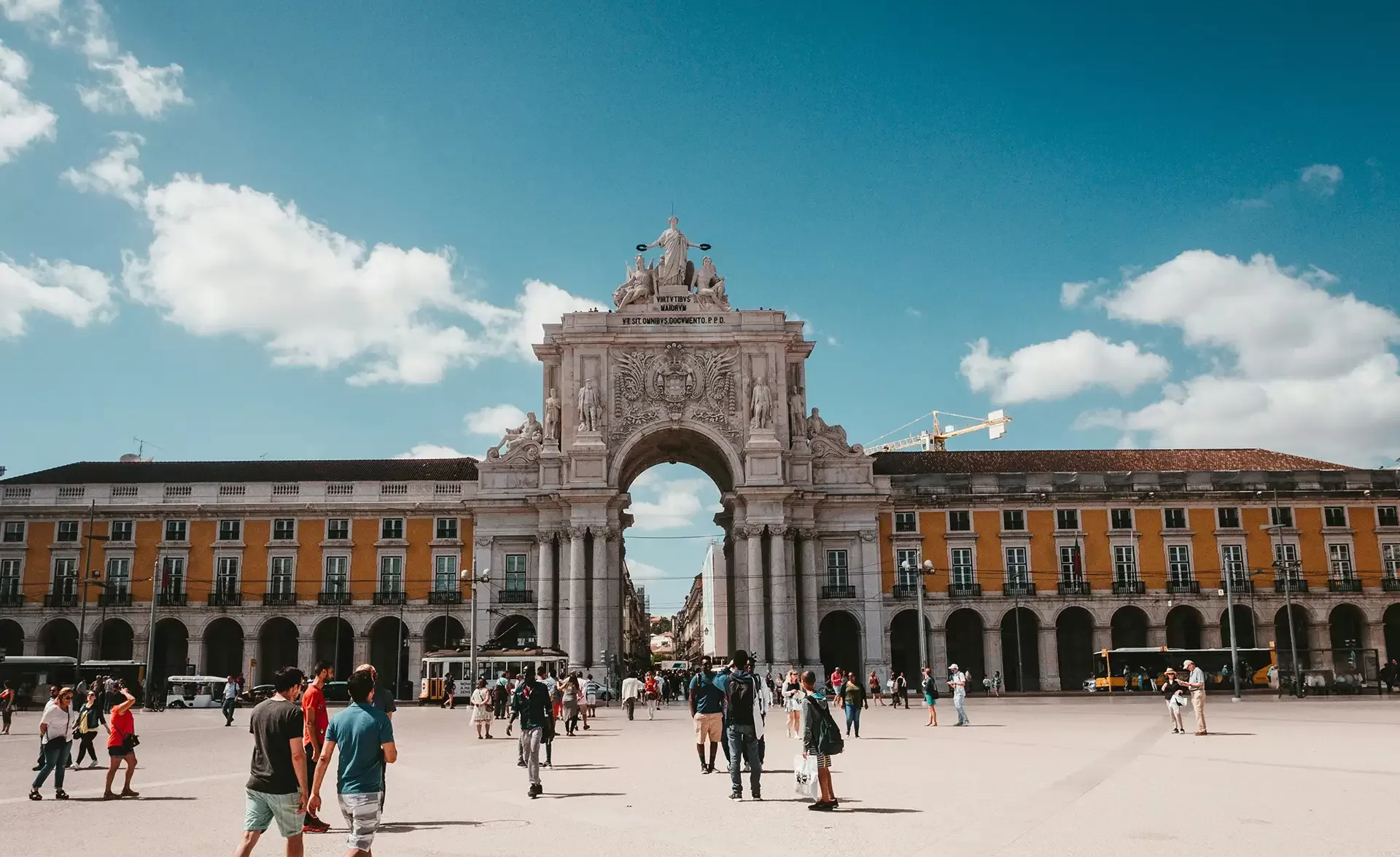 A scenic view of people walking towards a grand building with an arched walkway in Lisbon, showcasing its vibrant culture, historic architecture, and beautiful landscapes.