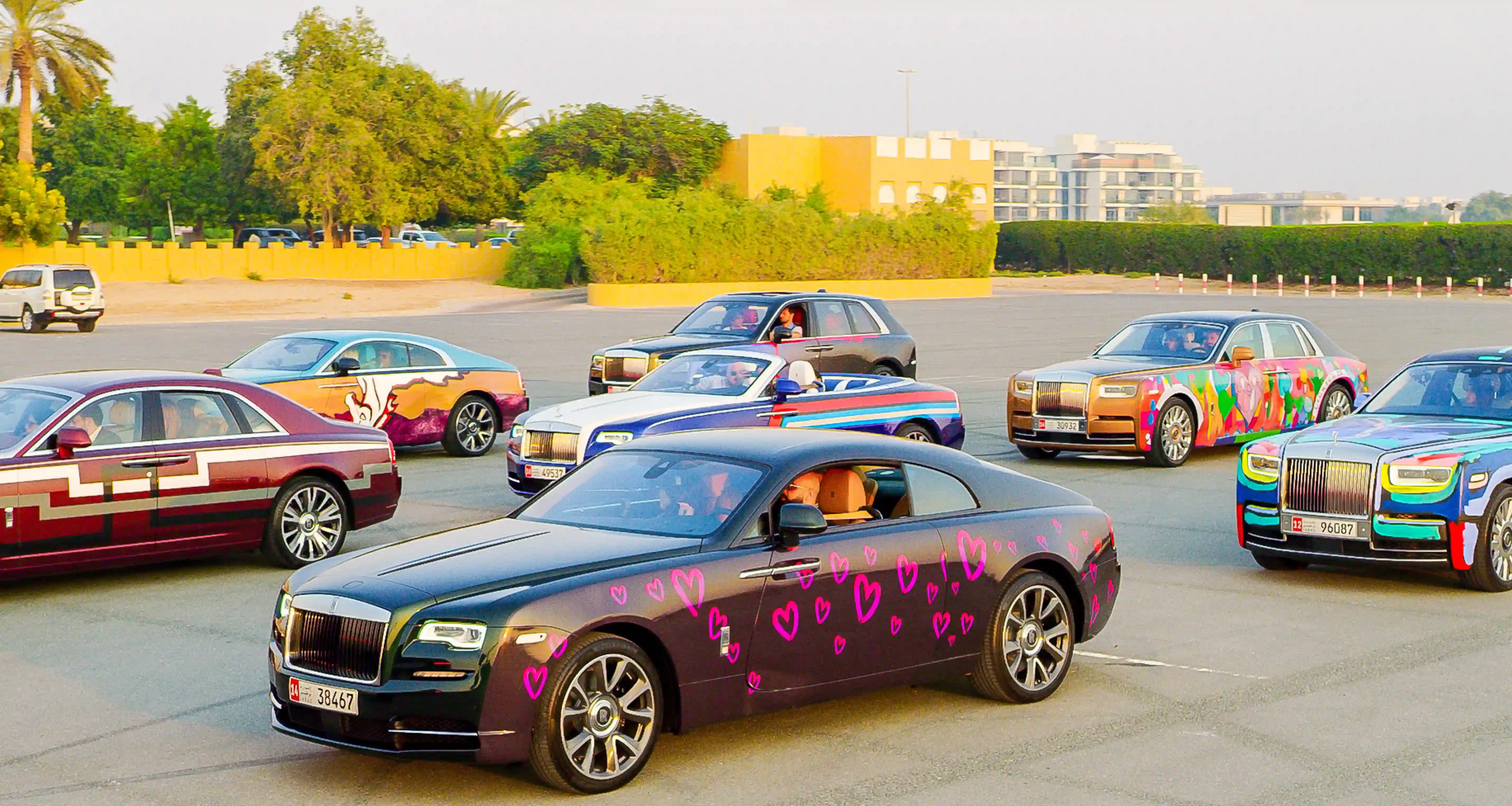Presentation of colorful spray-painted Rolls Royce cars on cement ground at sun set.