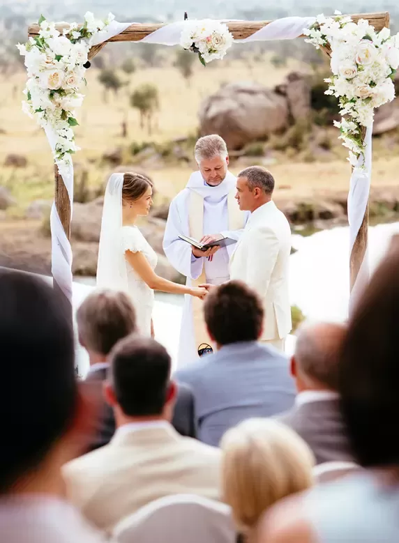 Bridge and groom holding hands down the aisle with the priest as viewers watch | Quintessentially Weddings