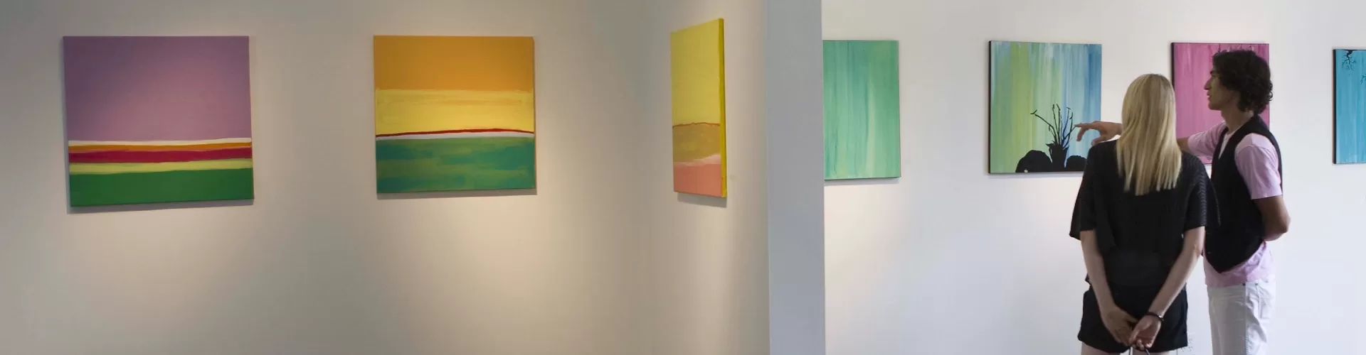 Two individuals observing artwork in a contemporary art gallery, engaged in thoughtful discussion about the pieces.