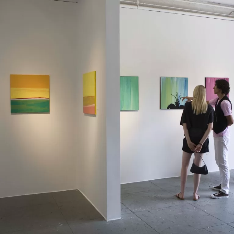 Two individuals observing artwork in a contemporary art gallery, engaged in thoughtful discussion about the pieces.