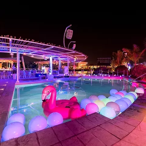 Swimming pool at night filled with balls and flamingo pool toys.