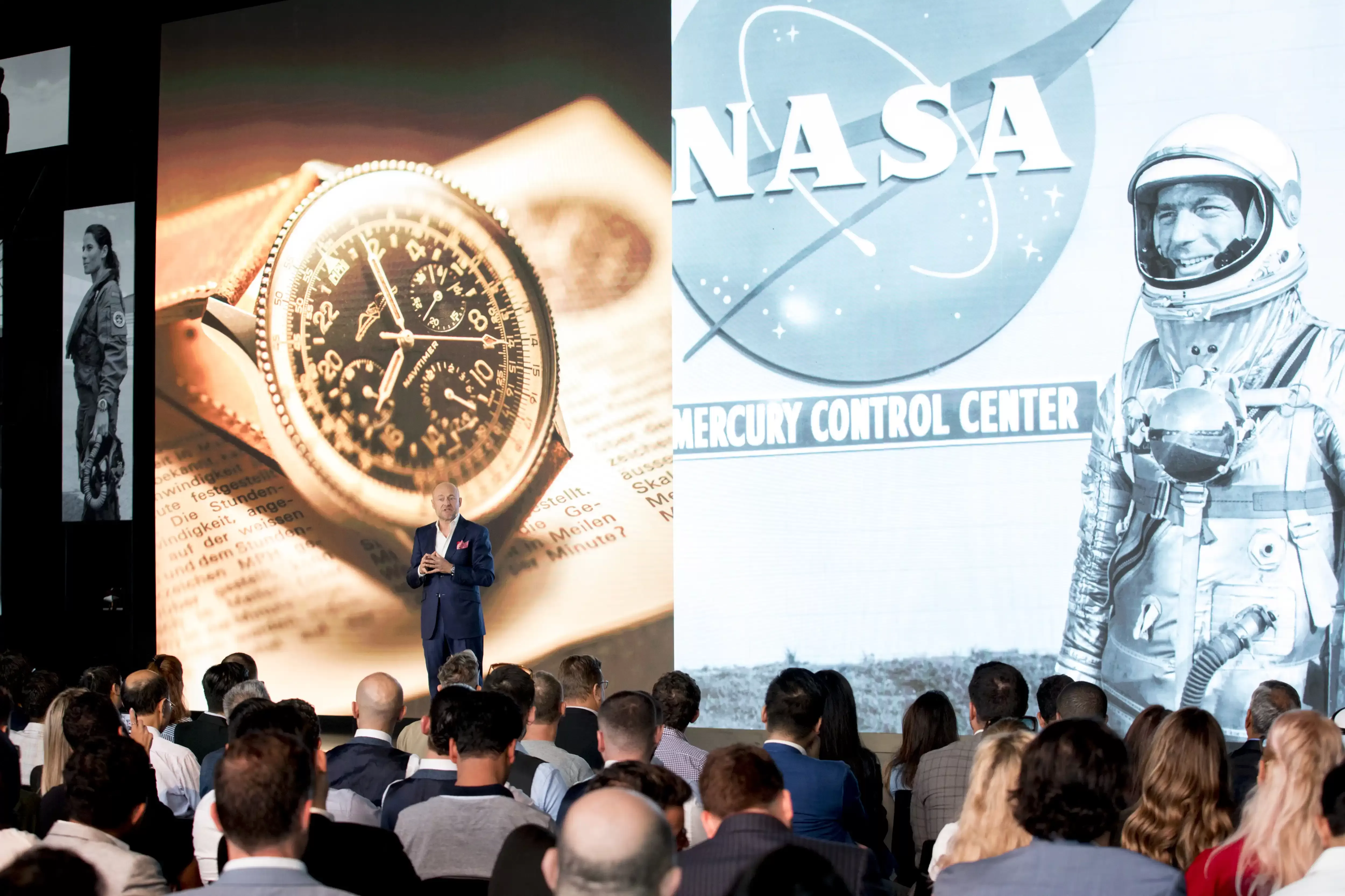 Man stood on stage in front of NASA picture screen talking to seated audience