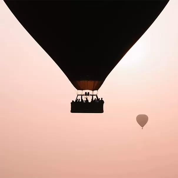 People on hot air balloon floating in pink sky
