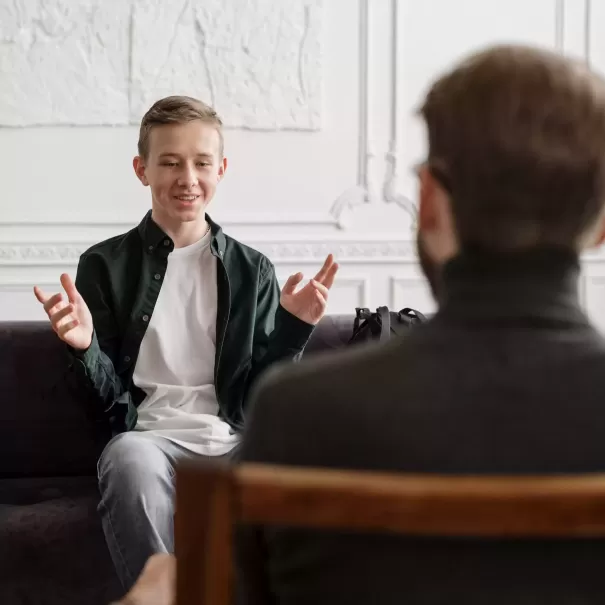 Boy sat on chair opposite adult on chair smiling making hand gestures