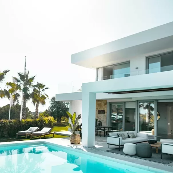 Luxury white villa with white exterior seating, palm trees and outdoor swimming pool
