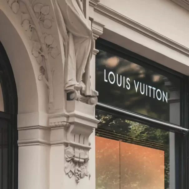 Front exterior of Louis Vuitton store, with branding on glass in between sculptured, ancient detailed white exterior building.