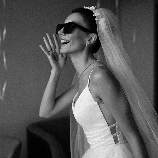 Fabulous young women in a wedding dress and vail smiling, posing and holding her hand up to her face wearing sunglasses