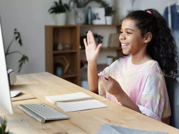 Girl student sat at a desk smiling at her MacBook with one hand in the air