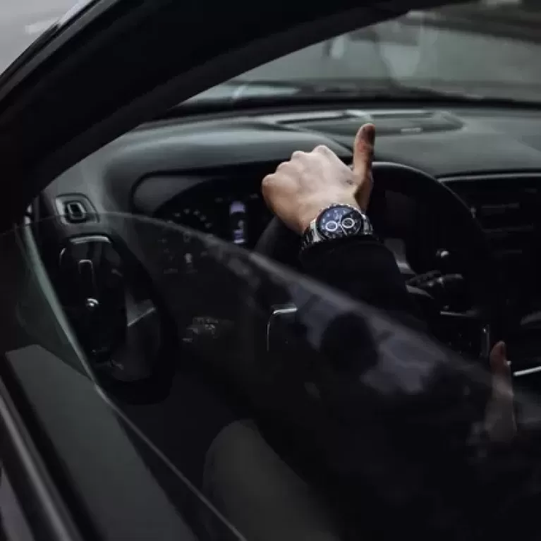 Close up of hand wearing a watch over steering wheel of car through the window.