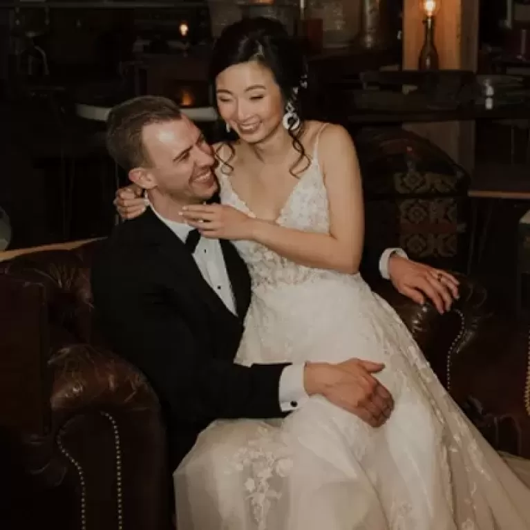 Women in wedding dress smiling and sat on lap of groom in a suit