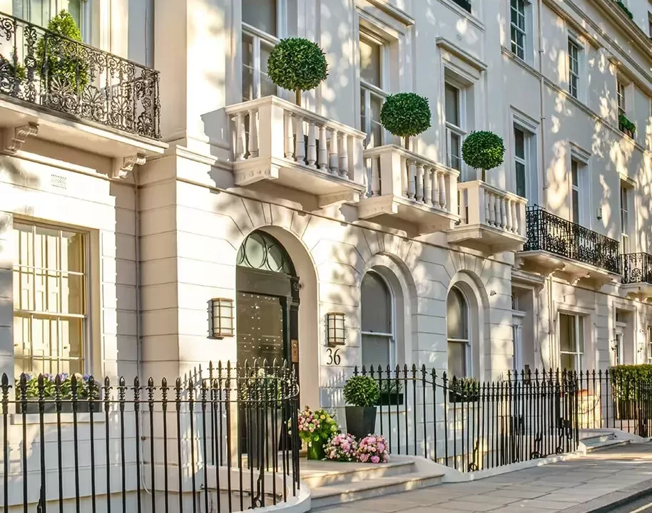 Exterior of beautiful white London town houses with balconies, black fencing and round wall hanging plants with arched door frames over black doors