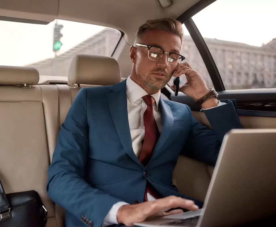 Smart man in a suit on the phone and on his laptop in the back of a fancy car