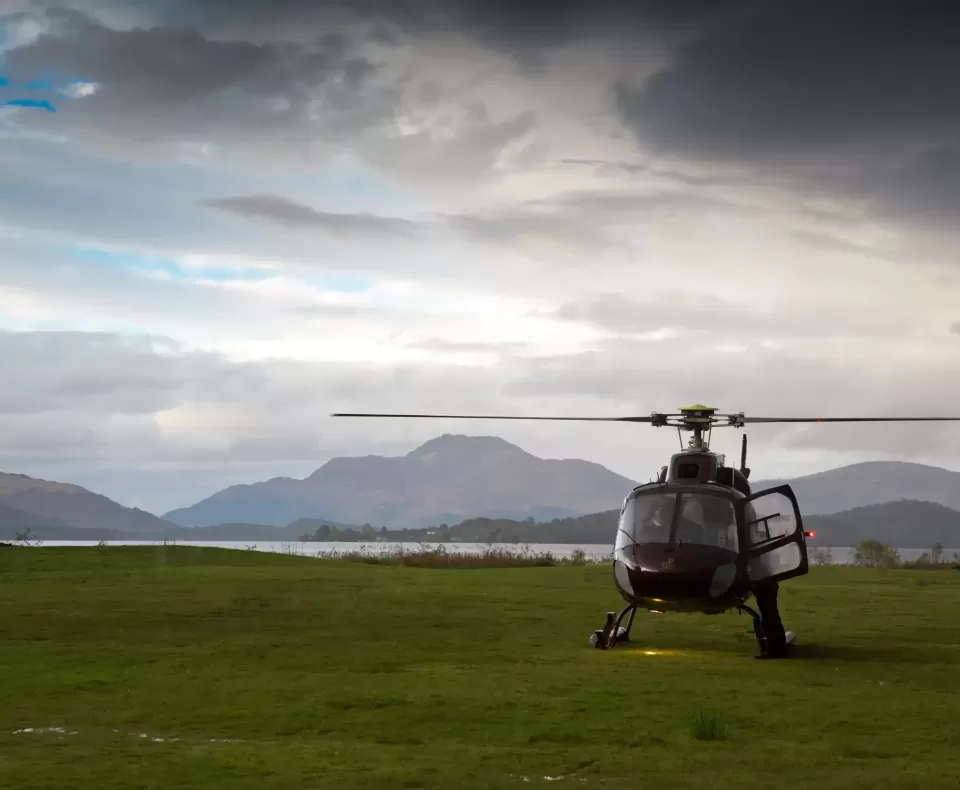 Helicopter on grass field with gloomy sky and mountain scenery