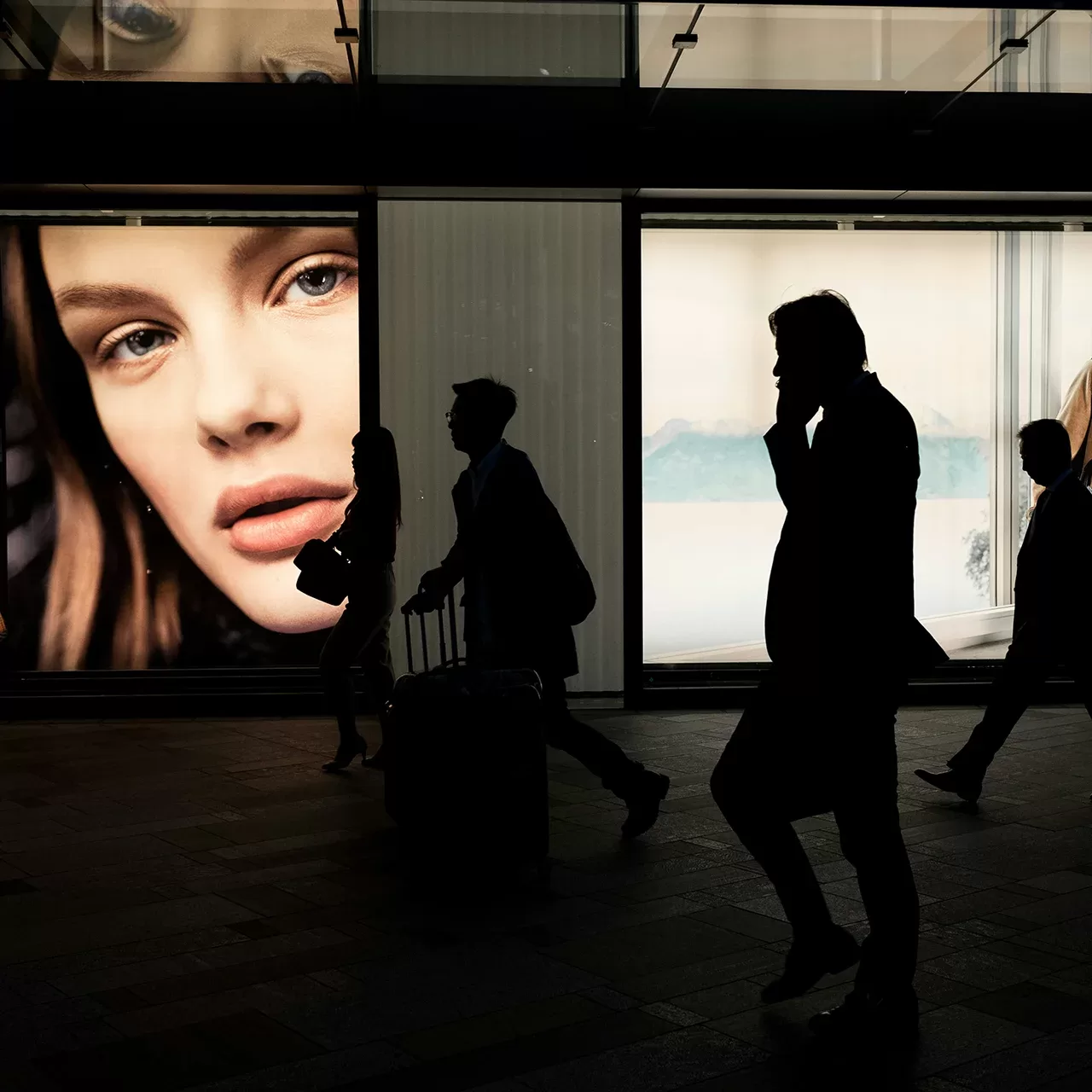 Black silhouettes of people walking in front of colourful adverts on a building