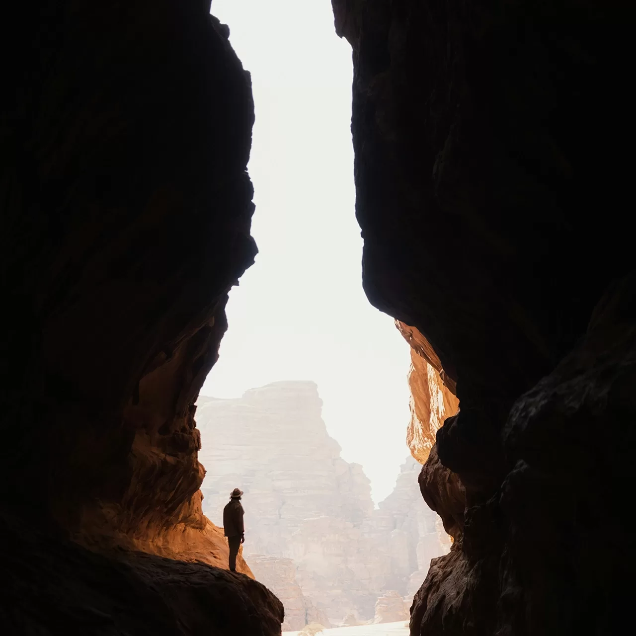 Photo of man standing on the ledge of a rock in between two giant mountainous rocks.