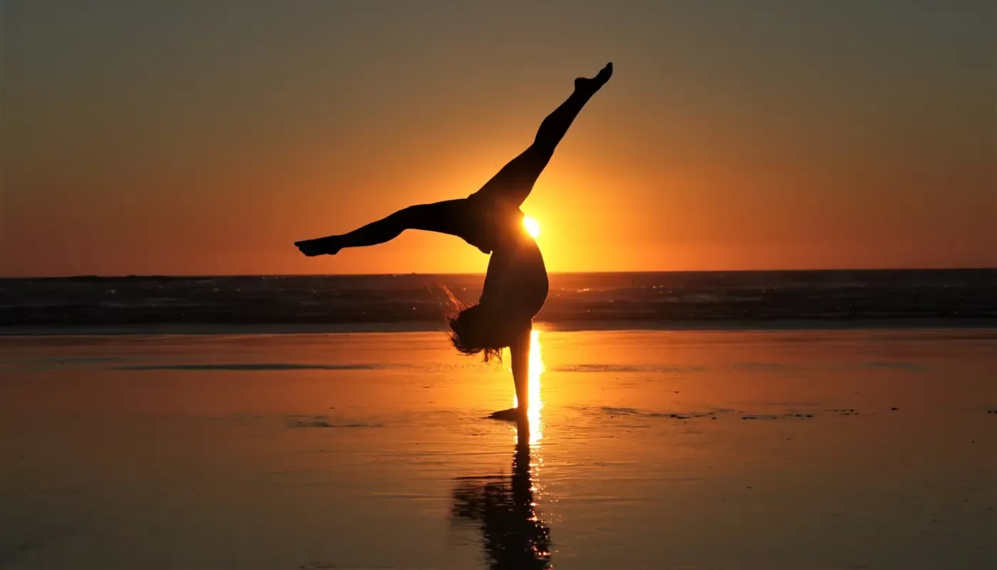Women in handstand yoga pose in the sea shore with the sunset behind her