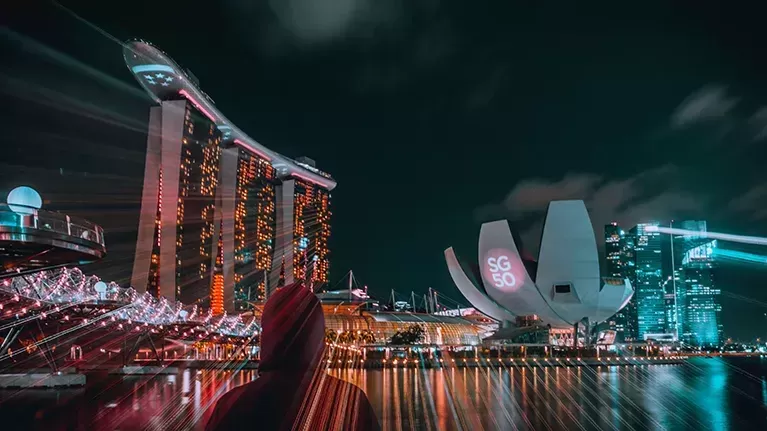Person wearing a red hoodie looking across the river at the lit up city of Singapore