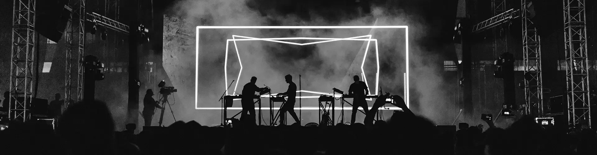 A monochrome photograph depicting a lively concert, featuring musicians on stage and an enthusiastic crowd.