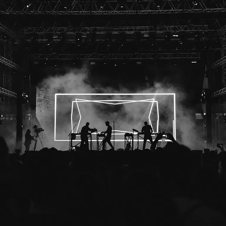 A monochrome photograph depicting a lively concert, featuring musicians on stage and an enthusiastic crowd.