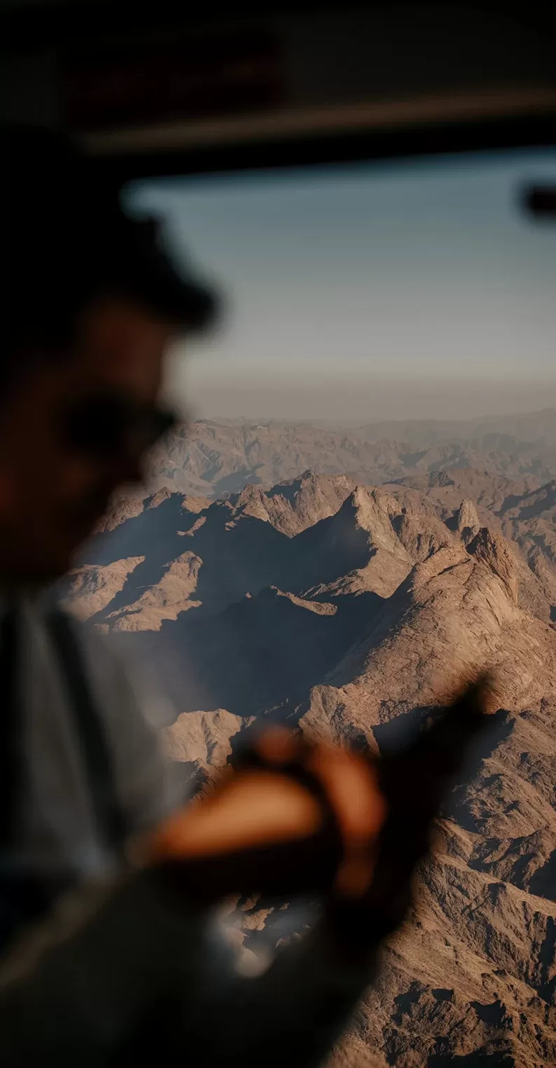 Man in a plane flying over rocky mountains in Alula, Saudi Arabia