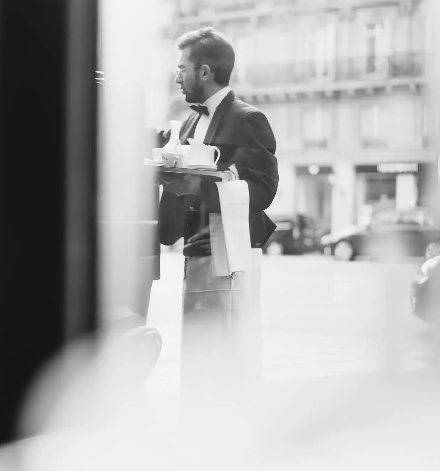 Black and white image of waiter in tuxedo serving coffee's outside